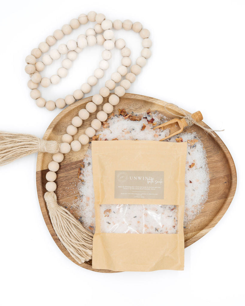 Wooden beads with tassel on a wooden tray with a bag of bath salts and a label.