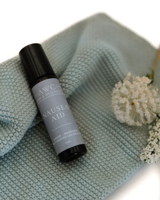Roll-on bottle labeled 'Nausea Aid' on a textured surface with flowers.