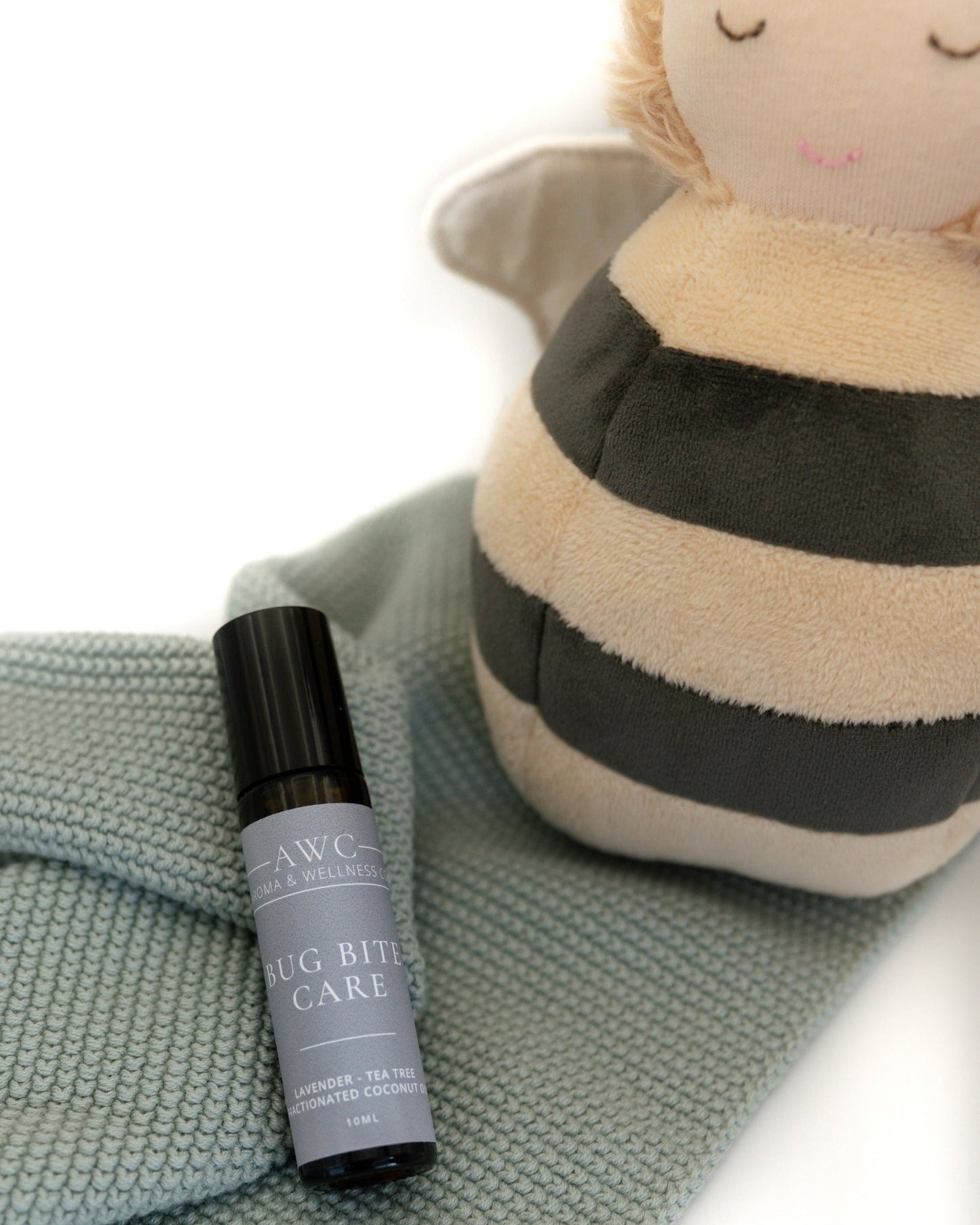 Small bottle labeled 'Bug Bite Care' next to a plush bee toy on a textured surface.