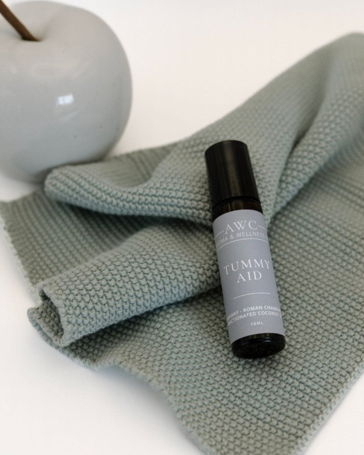 Skincare bottle labeled 'tummy Aid' on a textured green towel with an apple in the background.